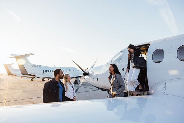 Two female passengers deplaning and being greeted by two people at the airstrip of an airport.